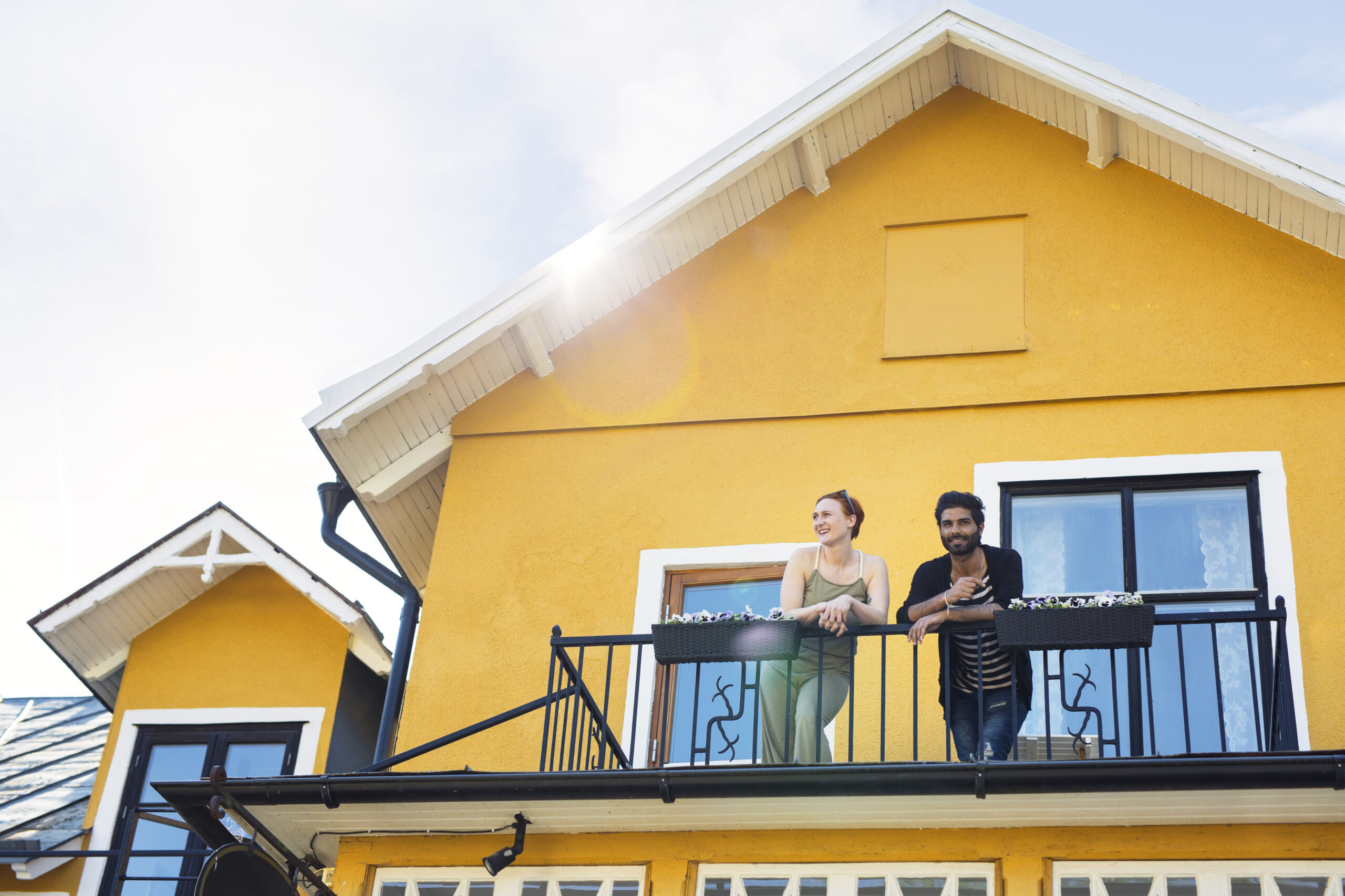 Smiling couple standing on the balcony of a vibrant yellow home, symbolizing successful home buying in Western New York